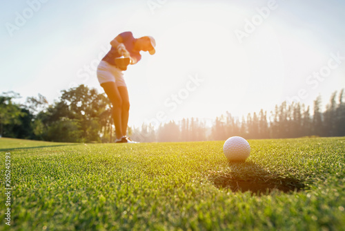 Golfer asian woman focus putting golf ball on the green golf on sun set evening time.. Healthy and Lifestyle Concept