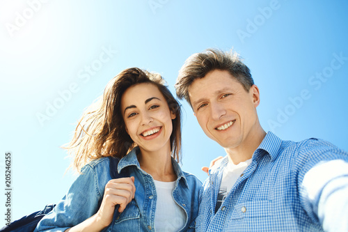 happy smiling couple, attractive man and woman looking in the camera at the sky background. bottom view