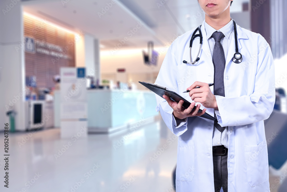 Smart male doctor wearing a medical suit hang on stethoscope and holding with blurred hospital in background. Doctor concept. Smart male doctor wearing a medical suit hang on stethoscope and holding with blurred hospital in background. Doctor concept.
