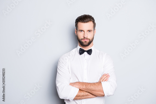 Bilde på lerret Portrait of serious handsome croupier in white shirt and bowtie having his arms