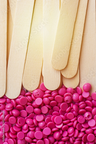 depilatory pearly pink solid wax beans and wooden stick background