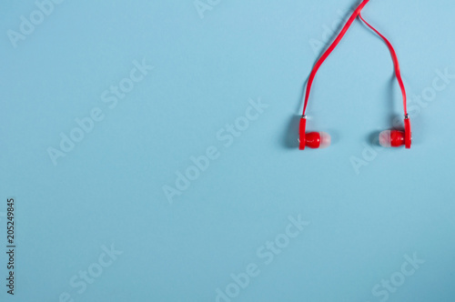 Red new earphone with cable on blue paper background with copy space