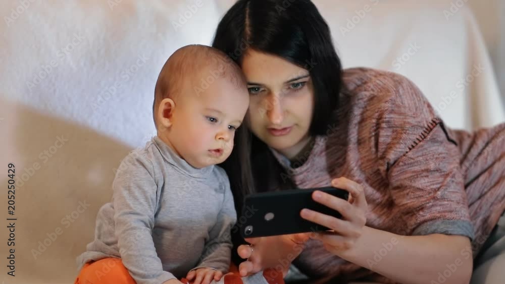 A young beautiful woman and a small child look closely at the screen of the smartphone slow motion shot.