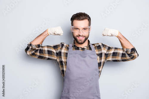Portrait of sportive athletic carpenter in safety glasses with hairstyle demonstrate his biceps with raised arms looking at camera isolated on grey background photo
