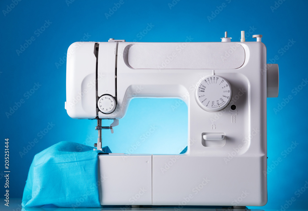 Sewing machine in work with fabric, on blue