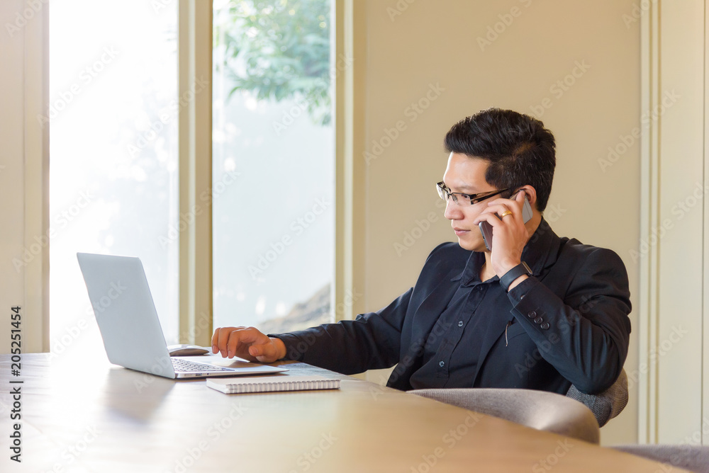 Smart handsome asian businessman in casual suit using laptop and smart phone for working at modern office or coffee shop cafe. Business and Office Concept. Smart handsome asian businessman in casual suit using laptop and smart phone for working at modern office or coffee shop cafe. Business and Office Concept.