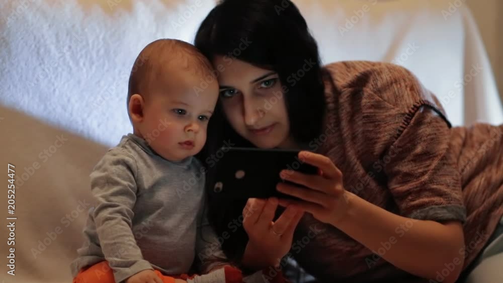 Young beautiful woman is showing the child a smartphone. The little boy looks closely at the image on the screen of the smartphone. Young beautiful woman is showing the child a smartphone. The little boy looks closely at the image on the screen of the smartphone.