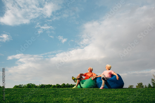 Senior couple sitting on beanbags on grass against the sky, and look to the side, low viewing angle.