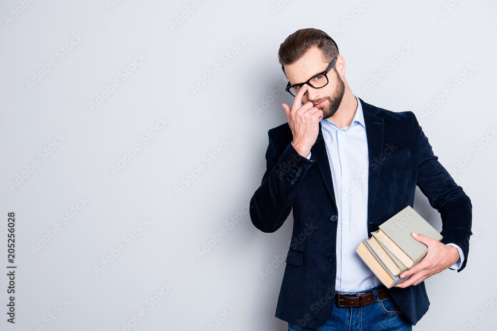 Portrait with copyspace, empty place of attractive stylish teacher fixing his glasses on face with finger, having books in hand, wearing shirt, jacket, jeans, isolated on grey background Portrait with copyspace, empty place of attractive stylish teacher fixing his glasses on face with finger, having books in hand, wearing shirt, jacket, jeans, isolated on grey background