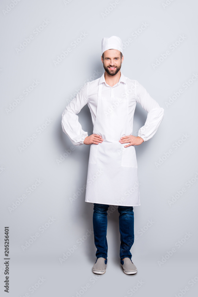 Full size body portrait of attractive handsome butcher isolated over grey background, wearing white shirt, apron, jeans, sneakers, holding arms on waist Full size body portrait of attractive handsome butcher isolated over grey background, wearing white shirt, apron, jeans, sneakers, holding arms on waist