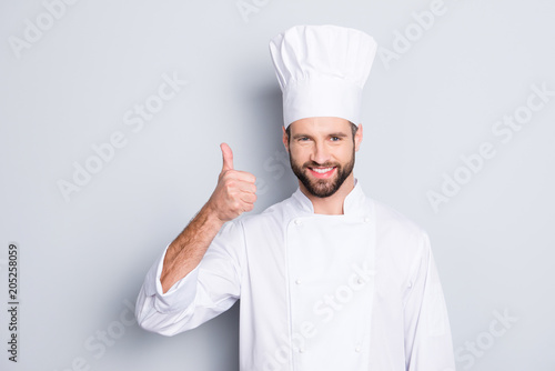 Portrait of cheerful joyful chef cook with stubble in beret, white outfit showing thumb up, approve menu, yes, done sign isolated on grey background, advertisement concept