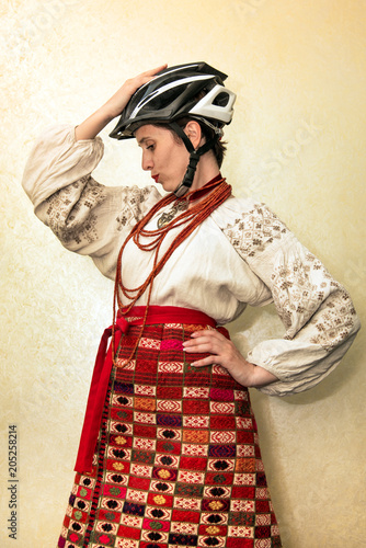 beautiful cheerful smile girl in traditional Ukrainian clothes (embroidery), an ancient chain, beads and a modern cycling helmet. photo