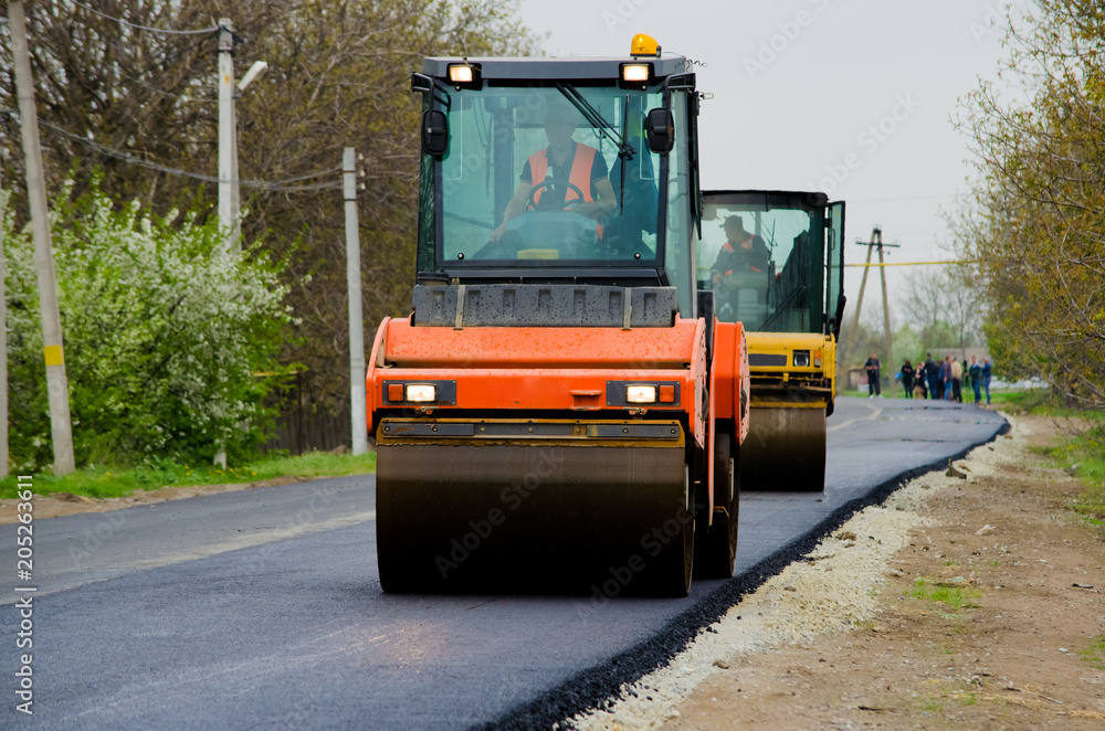 Vibration rollers closeup paving the road and laying asphalt in the village. Vibration rollers closeup paving the road and laying asphalt in the village.