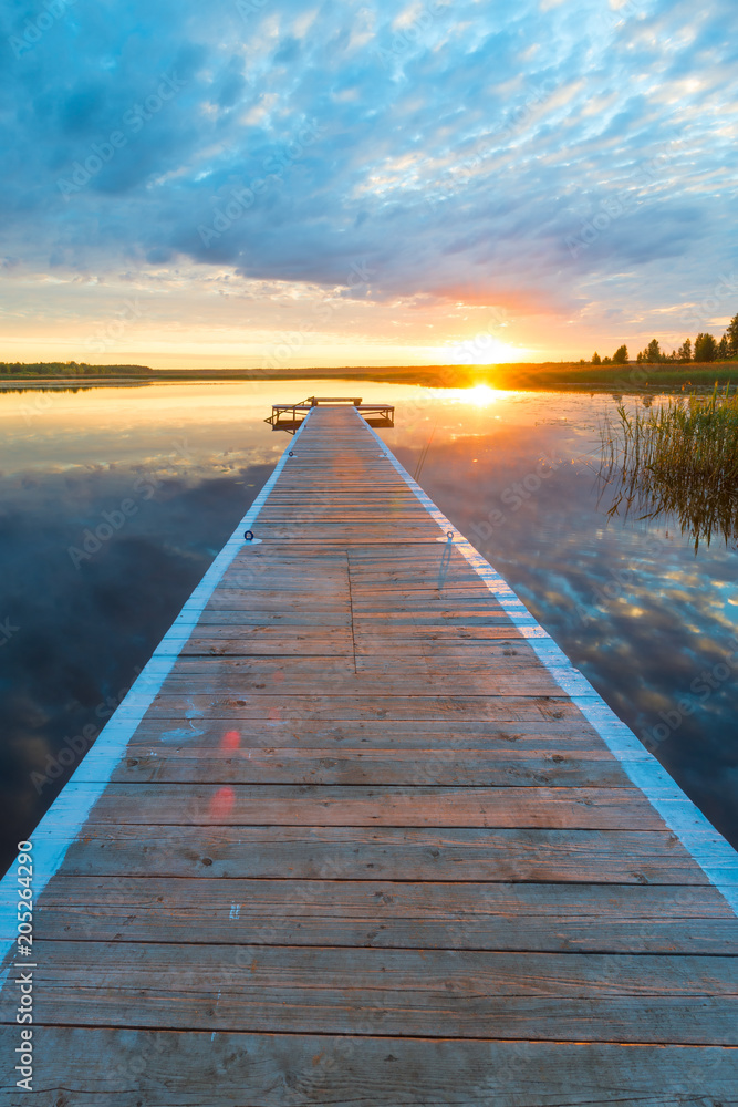 vertical photo of a beautiful landscape - a long wooden pier and a setting sun over a picturesque lake