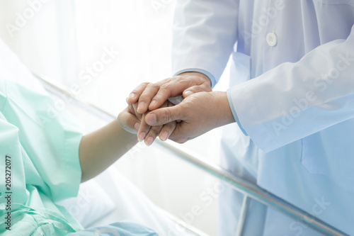 Doctor with patient. Routine health check and holding hands. Male medical doctor with young chinese woman.