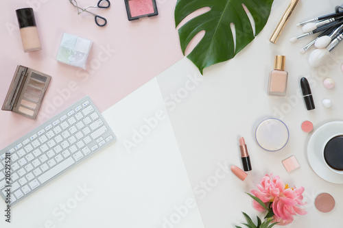 Pastel office table desk with computer laptop, green palm leaves, flowers, clipboard and beauty accessories, top view and flat lay. Home fashion women office workspace isolated on pink background.