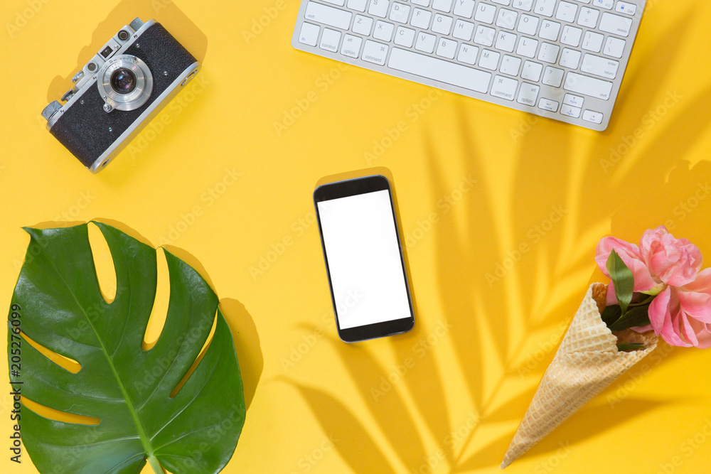 Flat lay on yellow background with mobile phone with white screen, palm leaf, vintage retro camera and peony flowers on waffle cone. Top view summer travel or vacation concept. Summer background. Flat lay on yellow background with mobile phone with white screen, palm leaf, vintage retro camera and peony flowers on waffle cone. Top view summer travel or vacation concept. Summer background.
