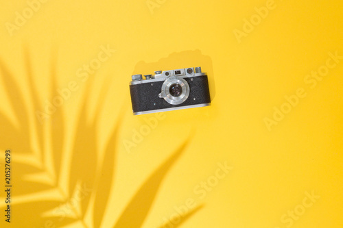 Top view of summer background with Tropical palm tree leaf shadow and vintage photo camera on a trendy bright yellow background, flat lay