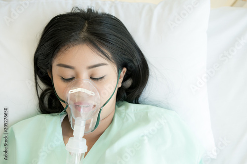 Young patient alone in bed. Sleeping in hospital bed. Oxygen mask on her face. Young beautiful chinese woman.