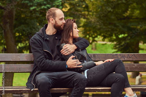 Attractive modern couple sitting on a bench in a park.