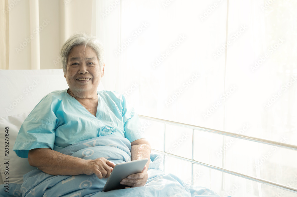 Elderly patient using tablet in bed. Elderly chinese woman in hospital bed using tablet to connect with her relatives. Connected world concept.