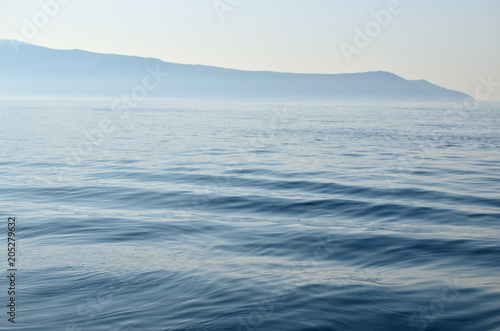 Calm sea surface with a land in a distance with a morning mist