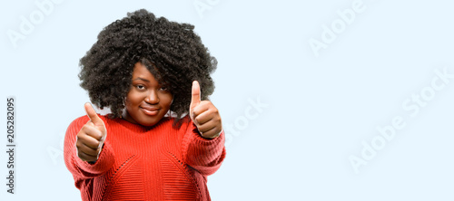 Beautiful african woman stand happy and positive with thumbs up approving with a big smile expressing okay gesture, blue background