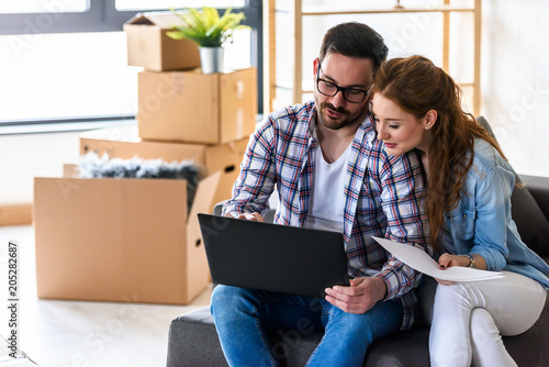 Young couple moving in new home. Sitting and relaxing after unpacking. Searching home decorating ideas on laptop.