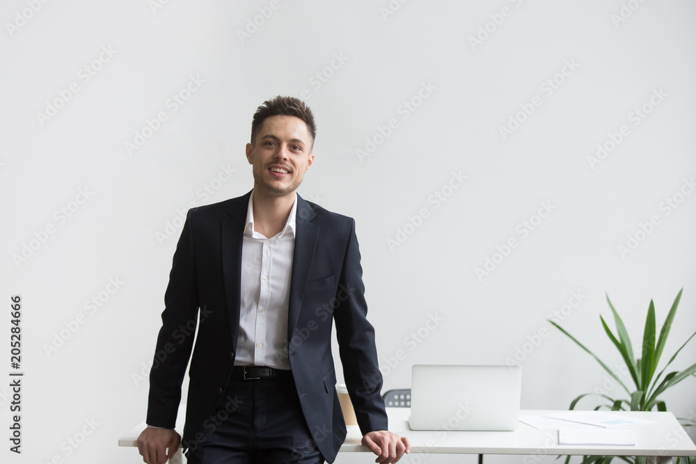 Smiling company CEO leaning back at office table posing near desk looking at camera satisfied with successful business. Concept of confidence, achievement, rewarding Smiling company CEO leaning back at office table posing near desk looking at camera satisfied with successful business. Concept of confidence, achievement, rewarding