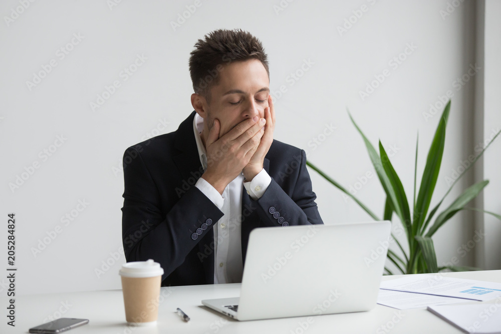 Tired bored office worker yawning working long hours at laptop in workspace. Exhausted workaholic being sleepy working late, drinking coffee. Concept of overwork, hardworking, boredom, no motivation Tired bored office worker yawning working long hours at laptop in workspace. Exhausted workaholic being sleepy working late, drinking coffee. Concept of overwork, hardworking, boredom, no motivation
