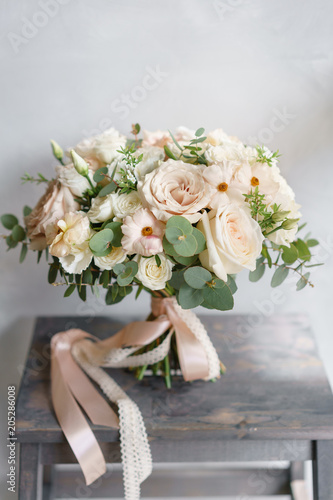 Fototapeta Naklejka Na Ścianę i Meble -  Wedding bouquet of white roses and buttercup on a wooden table. Lots of greenery, modern asymmetrical disheveled bridal bunch