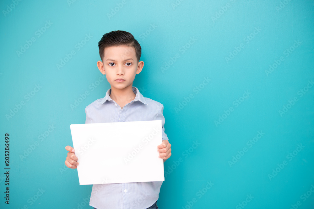 Young boy isolated in blue. Handsome early teenage boy portrait. Holding a white sign board, confident pose. Young boy isolated in blue. Handsome early teenage boy portrait. Holding a white sign board, confident pose.