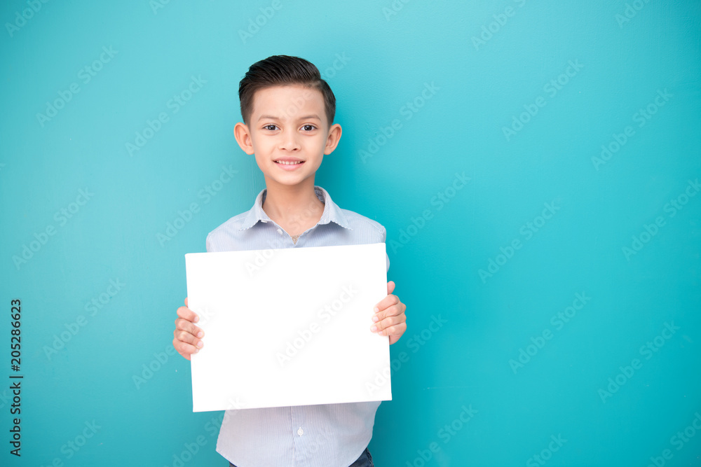 Young boy isolated in blue. Handsome early teenage boy portrait. Holding a white sign board, happy smile.