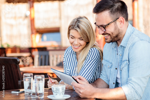 Happy young couple browsing online shop on a tablet  sitting in a cafe