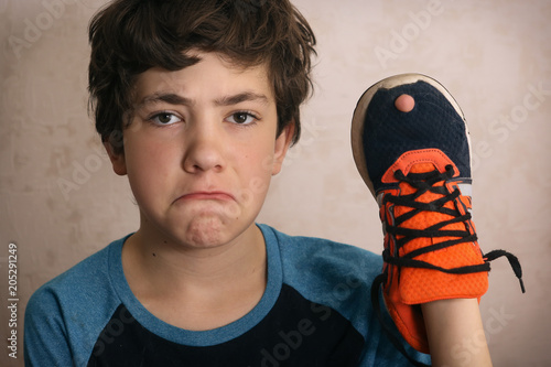 teenager boy frustrated about hole in his favourite trainers shoes close up portrait