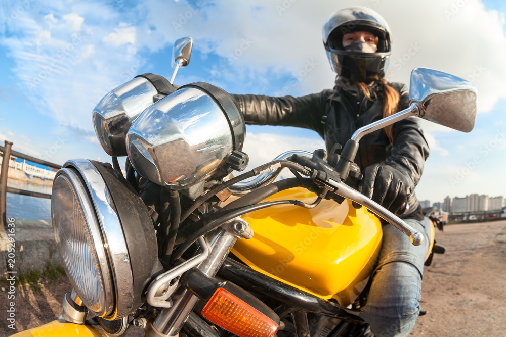 Wide angle view at young woman motorbiker sitting on bike, focus on headlight Wide angle view at young woman motorbiker sitting on bike, focus on headlight