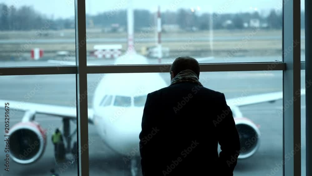 old Man stand at full height, gaze out airport terminal window, silhouette view. Looks at the plane at the airport old Man stand at full height, gaze out airport terminal window, silhouette view. Looks at the plane at the airport