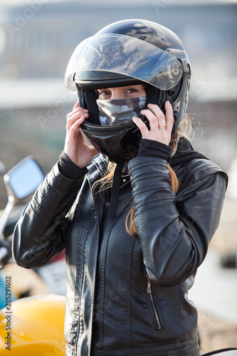 Young woman motorcyclist put on crash helmet for riding bike on urban road