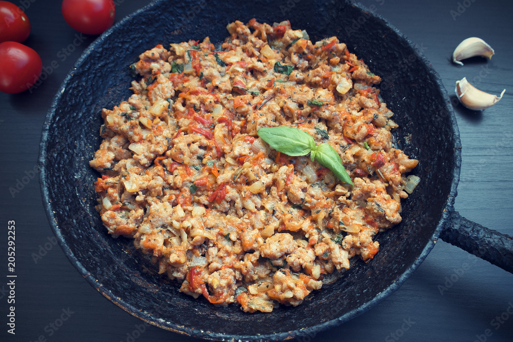 Fried ground meat with vegetables in an old frying pan on a dark background, garlic and tomatoes Fried ground meat with vegetables in an old frying pan on a dark background, garlic and tomatoes