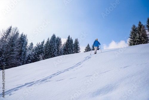 Hiker with snowshoes on snow trail in winter landscape of forest in Oberstdorf, Bavaria Alps in South of Germany. Beautiful landscape with coniferous trees and white snow. Winter sport activity.