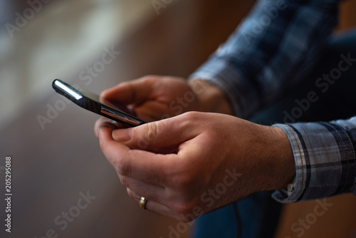 Man wearing checkered shirt and holding  texting  smartphone  close up.