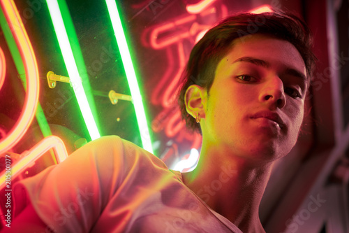 Young man, lit by neon light at night.