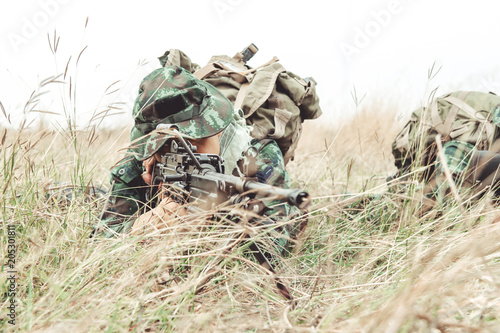 Soldier hiding in bushes ready to shoot. Ambush his ememy, ready his assault rifle. Hiding below the tree line. Military combat training concept. © Baan Taksin Studio