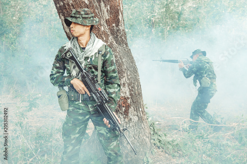 Soldier standing behind a tree ready to attack. Chinese male soldier standing behind a large tree looking around for his ememy and covering his friend. Smoke effect.