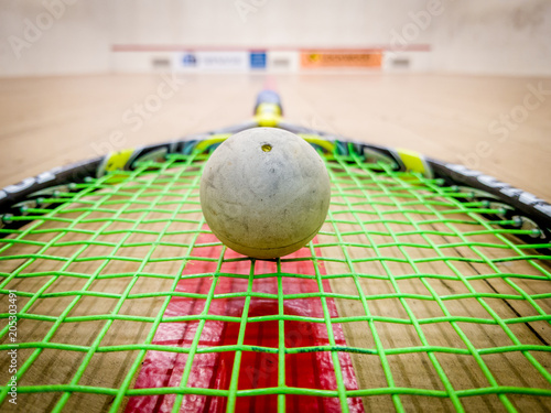 White squash ball on the strings of a racket in the middle of a indoor squash court
