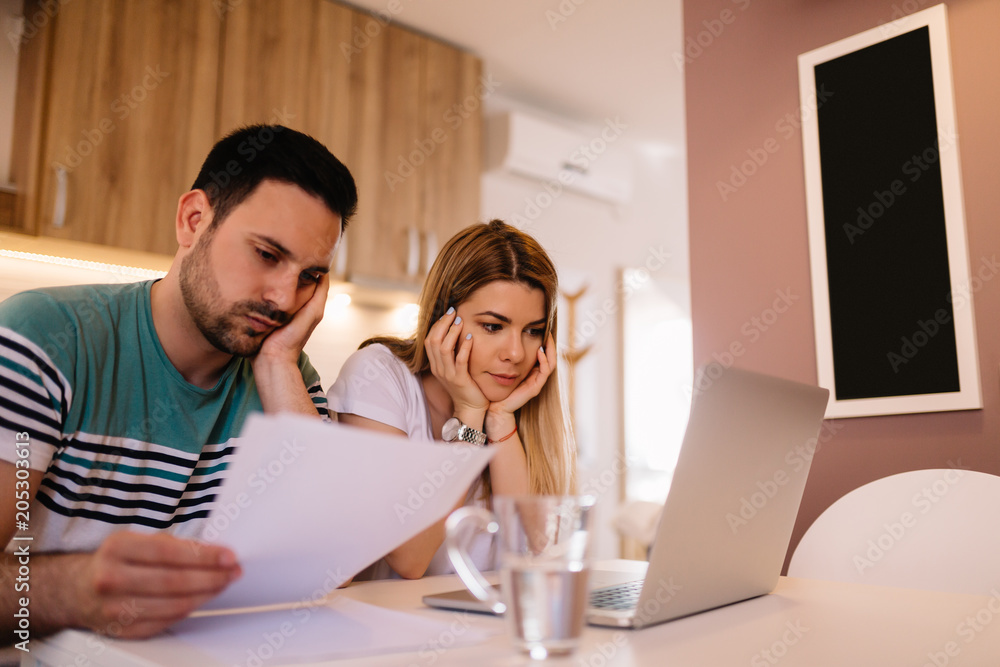 Worried young couple analyzing bills while sitting in kitchen Worried young couple analyzing bills while sitting in kitchen