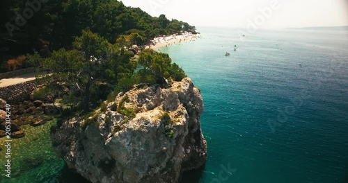 aerial shot of the famous little paradise rockisland in brela / croatia / europe. super wide shot, camera moves upwards and tilts down with straight focus on the island. in the background the beach photo