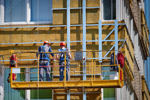 Fotografie, Obraz Professional construction Workers on the scaffold elevator insulated wall façade with mineral wool