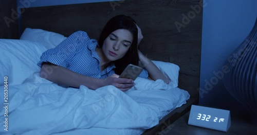 Portrait of the young woman lying in the bed late atnight and using a smartphone in her hands as having an insomnia. Indoors photo