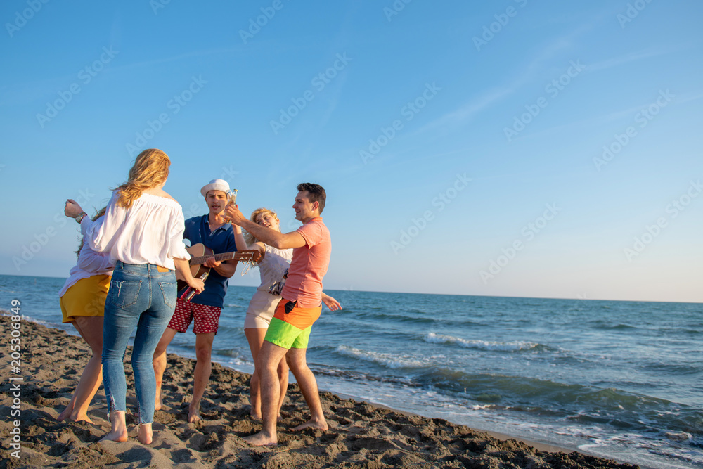 group of happy young people dancing at the beach on beautiful summer sunset